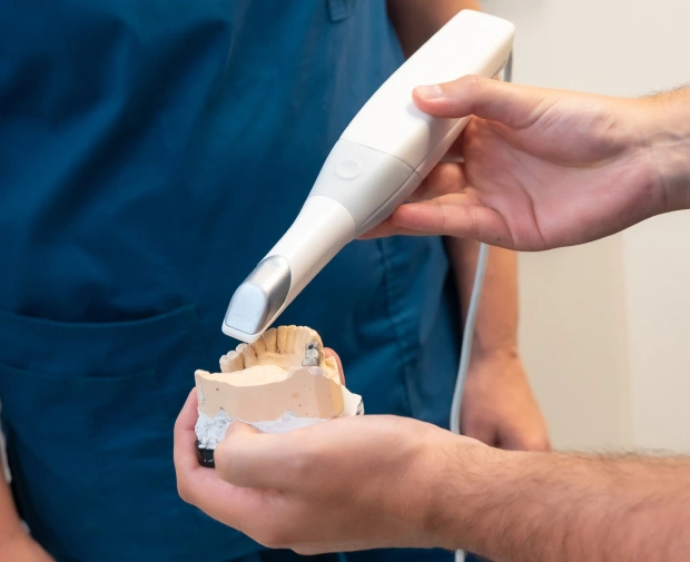 A close‑up of a dental professional using a handheld intraoral camera device to scan a dental model of teeth in Bedford